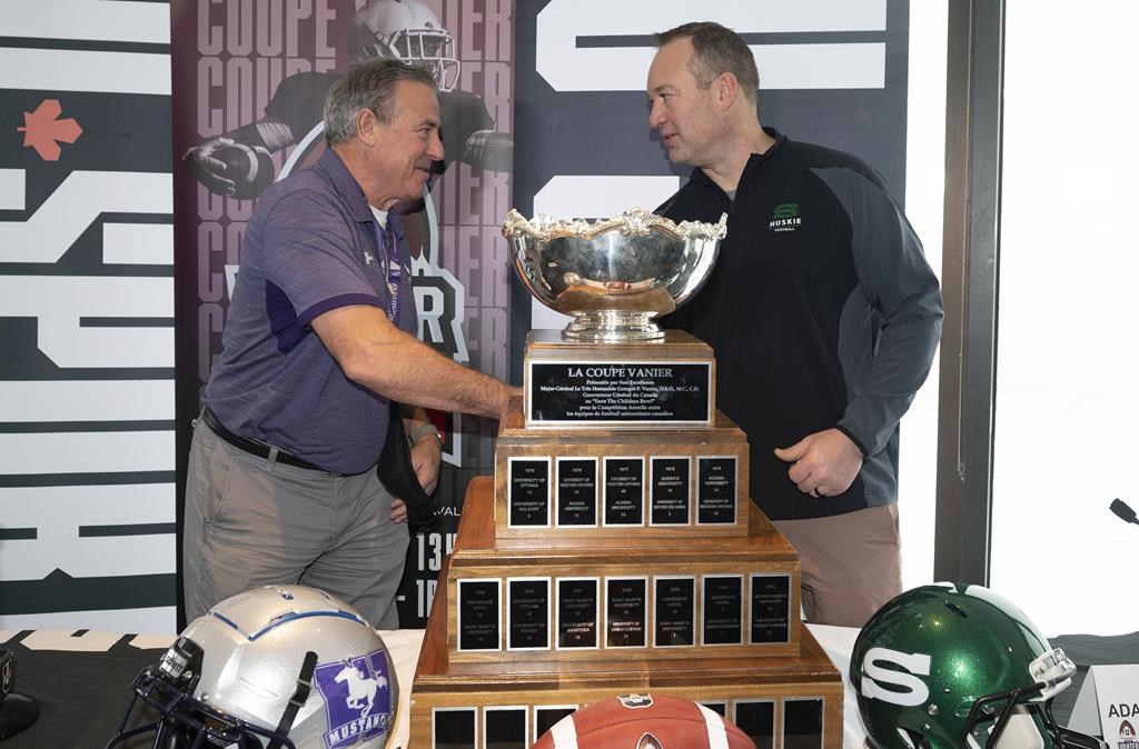 Western University Mustangs head coach Greg Marshall, left, shakes hand with Saskatchewan University Huskies head coach Scott Flory, while standing behind the Vanier Cup trophy, in Quebec City, Thursday, Dec. 2, 2021.
