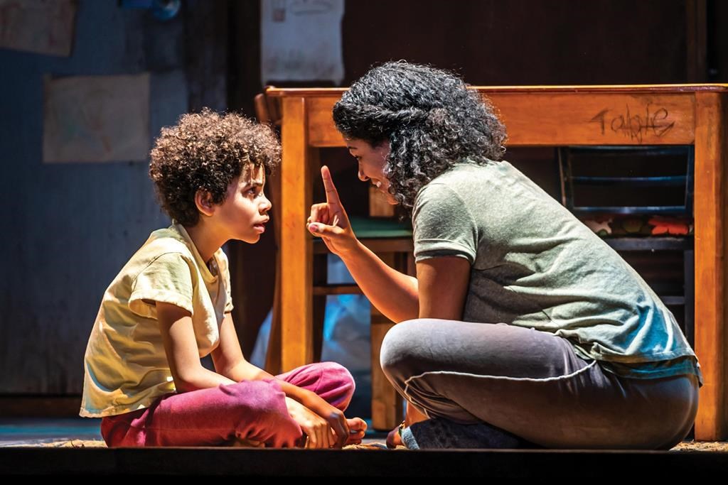 Photo of an actress and young actor sitting down on stage performing.