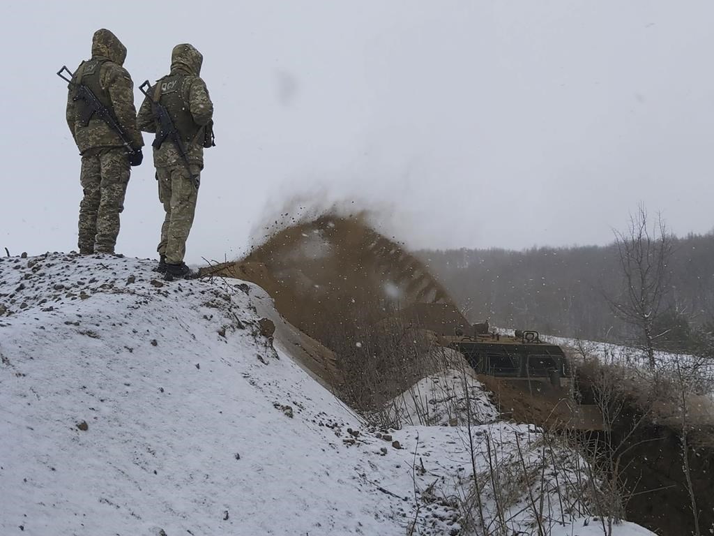 In this image provided by the Ukrainian Board Guard Press Office, Ukrainian border guards watch as a special vehicle digs a trench on the Ukraine-Russia border close to Sumy, Ukraine, Tuesday, Dec. 21, 2021. (Ukrainian Board Guard Press Office via AP)