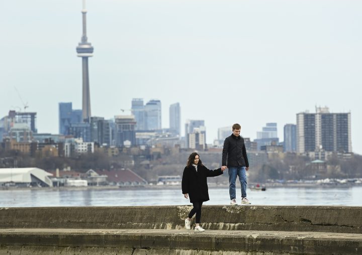 People hold hands overlooking the city skyline on a calm Lake Ontario near Humber Bay in Toronto on Monday, April 5, 2021.