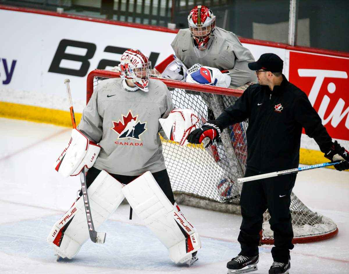 Goalie Dylan Garand, left, and goalie Sebastian Cossa, centre, listen to goaltending coach Olivier Michaud during a practice at the Canadian World Junior Hockey Championships selection camp in Calgary, Thursday, Dec. 9, 2021.
