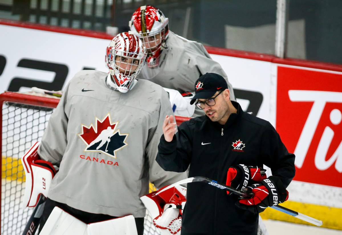 Goalie Dylan Garand, left, and goalie Sebastian Cossa, centre, listen to goaltending coach Olivier Michaud during a practice at the Canadian World Junior Hockey Championships selection camp in Calgary, Thursday, Dec. 9, 2021.