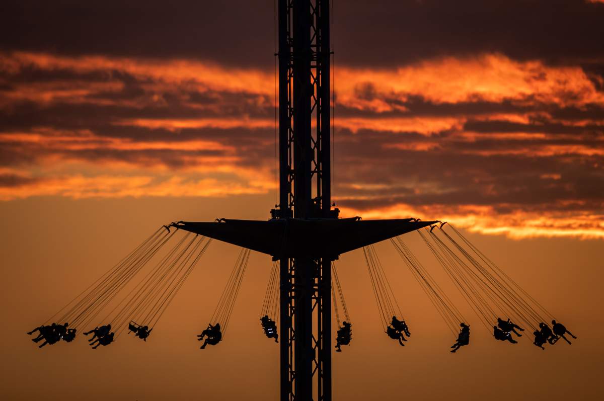 People are silhouetted while riding the Atmosfear double swing, which lifts riders more than 66 metres into the air while spinning at up to 70 km/h, at the Pacific National Exhibition at sunset in Vancouver, on Tuesday, August 31, 2021.