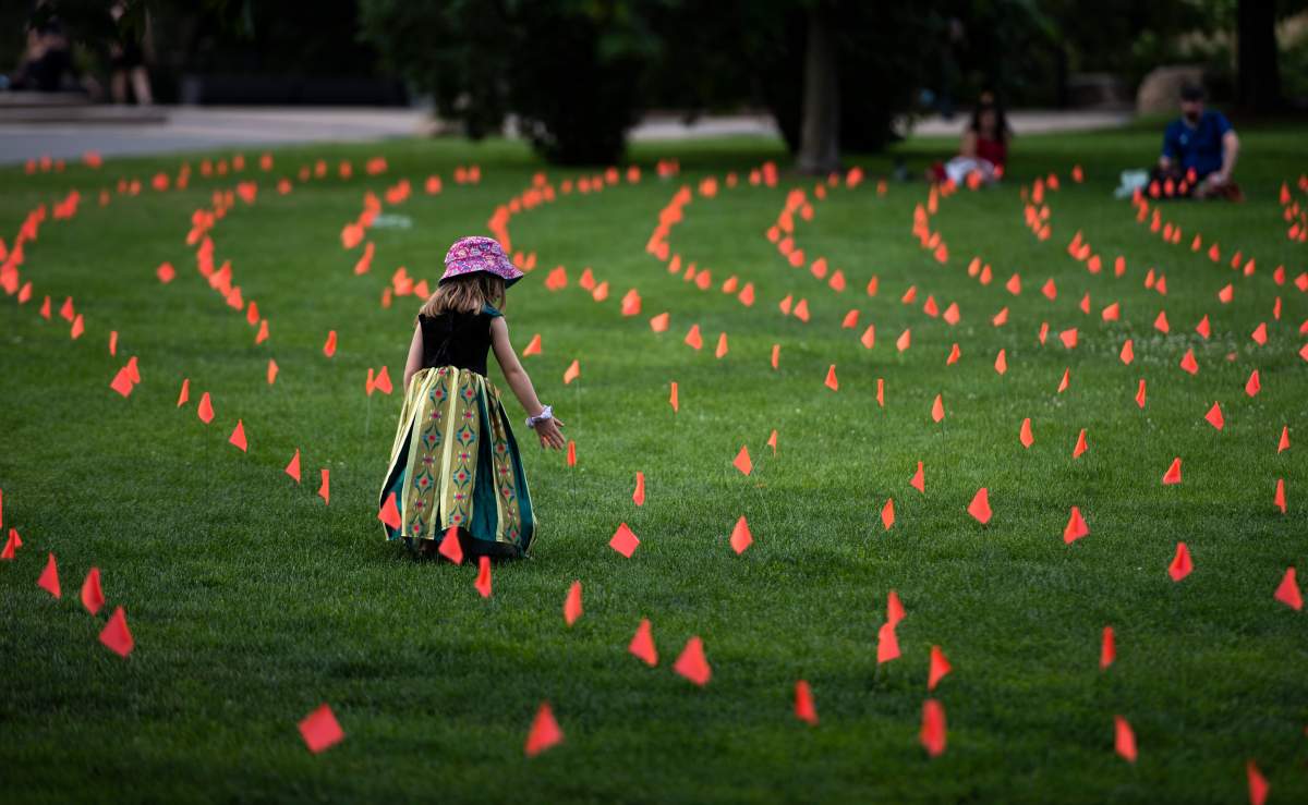 Margot King, 4, touches an orange flag, representing children who died while attending Indian Residential Schools in Canada, placed in the grass at Major's Hill Park in Ottawa, on Canada Day, Thursday, July 1, 2021.