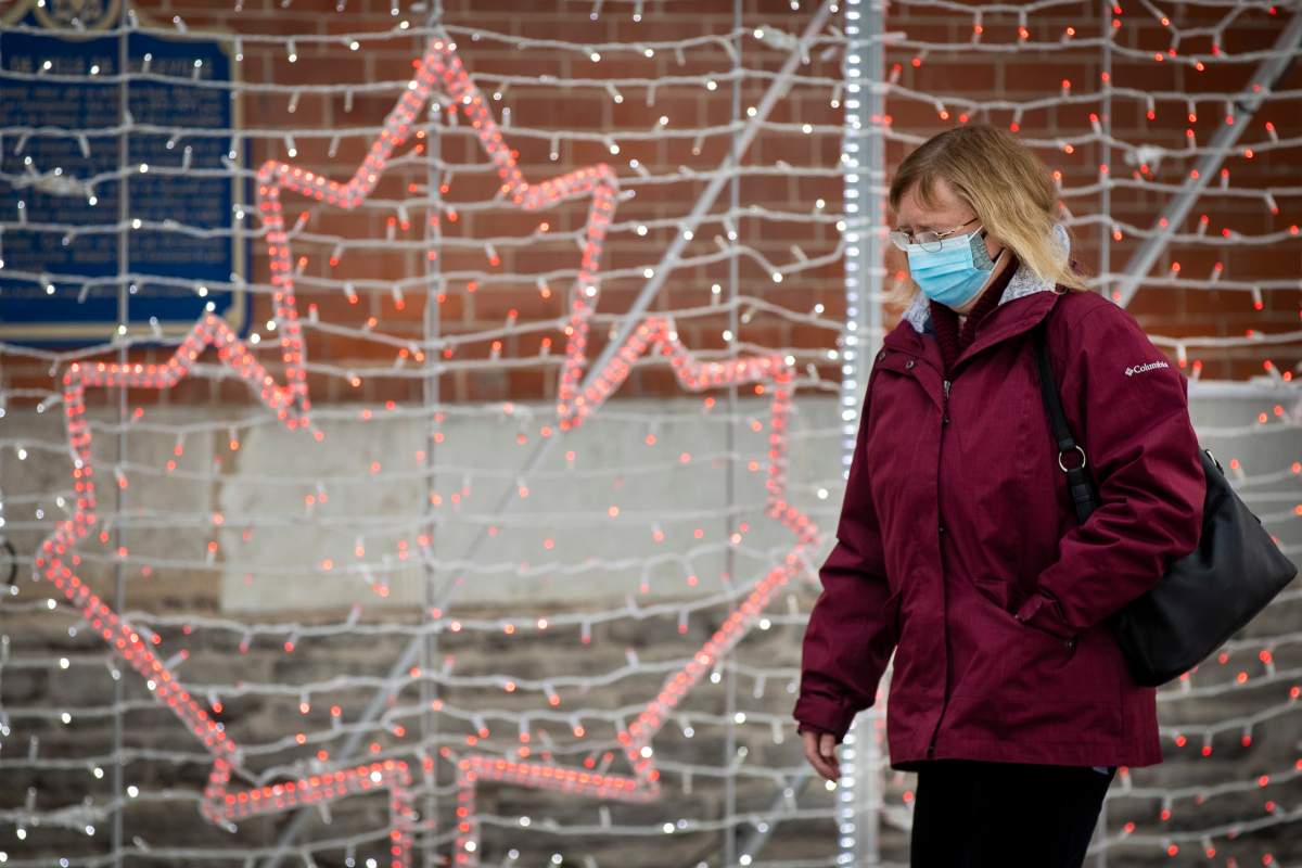A person wears a surgical mask to protect them from the COVID-19 virus while walking past an illuminated maple leaf.