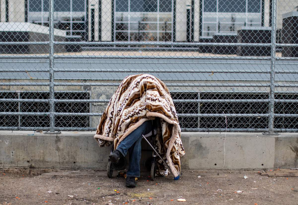 A homeless person stays warm while covered up with a blanket sitting by outdoor heat vents in Edmonton, Thursday, Dec. 9, 2021.