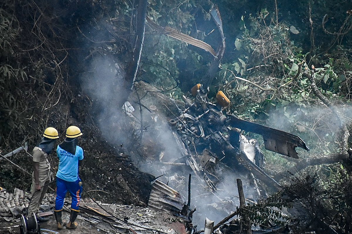 Firemen and rescue workers stand next to the debris of an IAF Mi-17V5 helicopter crash site in Coonoor, Tamil Nadu, on December 8, 2021.