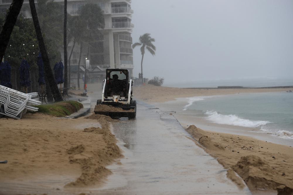 A small tractor pushes sand off a walkway on Waikiki Beach, Monday, Dec. 6, 2021, in Honolulu.