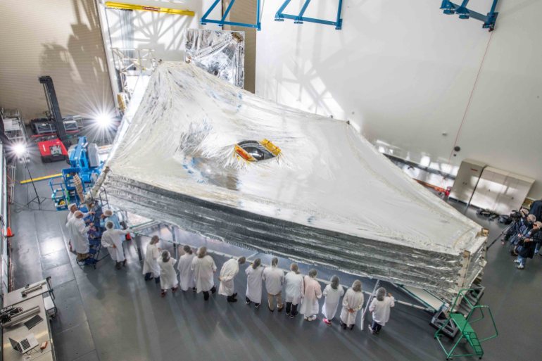 Scientists surround a full-sized replica of JWST’s five-layer sunshield, which is the largest part of the observatory