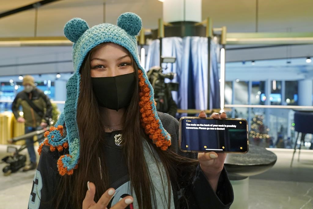 Seattle Kraken fan Nadia Popovici poses for a photo before an NHL hockey game between the Kraken and the Vancouver Canucks, Saturday, Jan. 1, 2022, in Seattle. Popovici is showing the text of a message she showed to Canucks assistant equipment manager Brian “Red” Hamilton on Oct. 23, 2021, as she sat behind the Canucks’ bench during the Kraken’s home-opener hockey game. (AP Photo/Ted S. Warren)