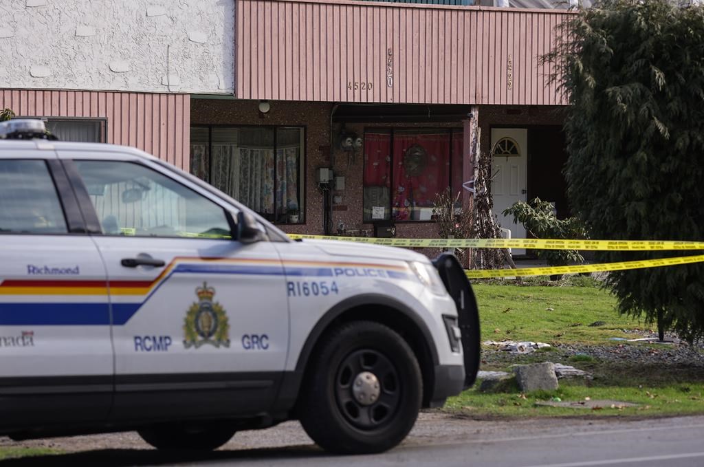 An RCMP officer sits outside a home surrounded by police tape where four people were found dead Tuesday, in Richmond, B.C., on Wednesday, January 26, 2022. The Integrated Homicide Investigation Team says one of the people found dead in a Richmond, B.C., home had a valid firearms licence and access to guns. 