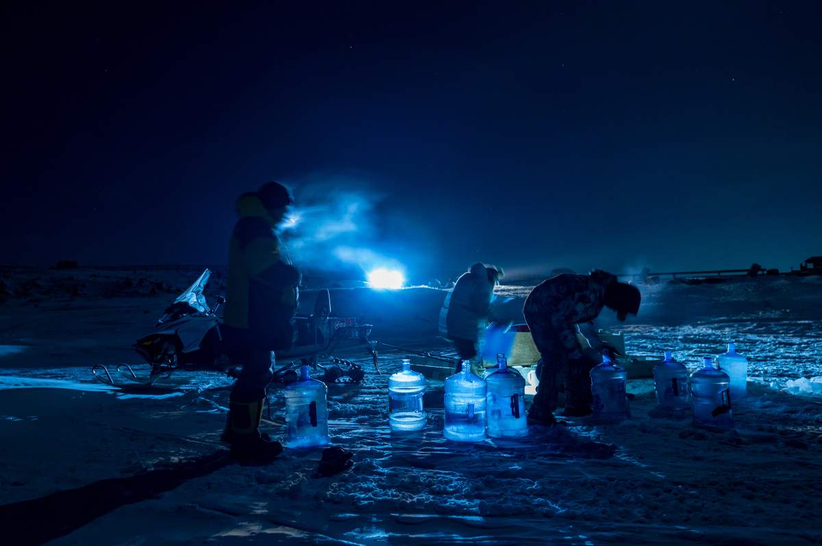 Residents of Iqaluit collect river water through holes carved into the ice near Iqaluit, Nunavut., on Friday, Jan 14, 2022. (THE CANADIAN PRESS/Dustin Patar)