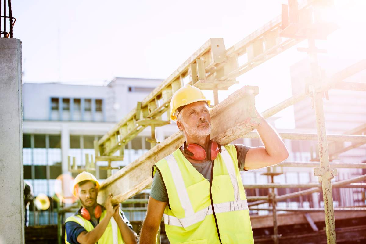 Construction workers carrying plank at site