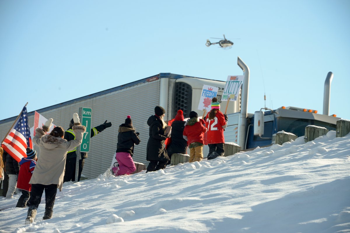 Quebec Provincial Police keep an eye on people standing on the Trans Canada highway between Montreal and Ottawa as they wait for a convoy protesting federal vaccine mandates to pass through Rigaud, Que., Friday, Jan. 28, 2022.