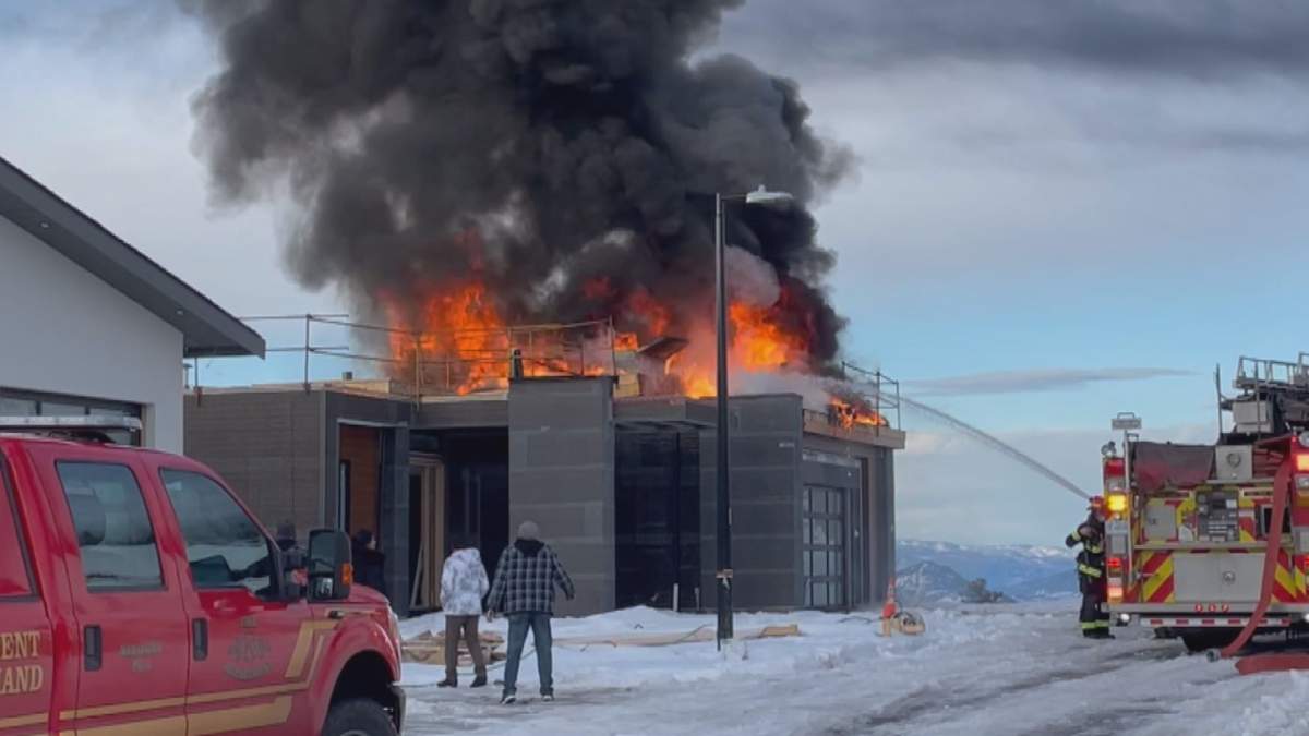 The fire deparment sprays water on a burning building under construction as people look on.