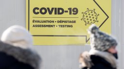 A COVID-19 testing sign and two people walking in front of it.
