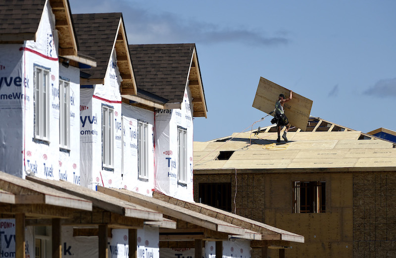A builder carries a sheet of wood on the roof of a home in a new subdivision in the Ottawa suburb of Kanata, on Friday, July 30, 2021. 