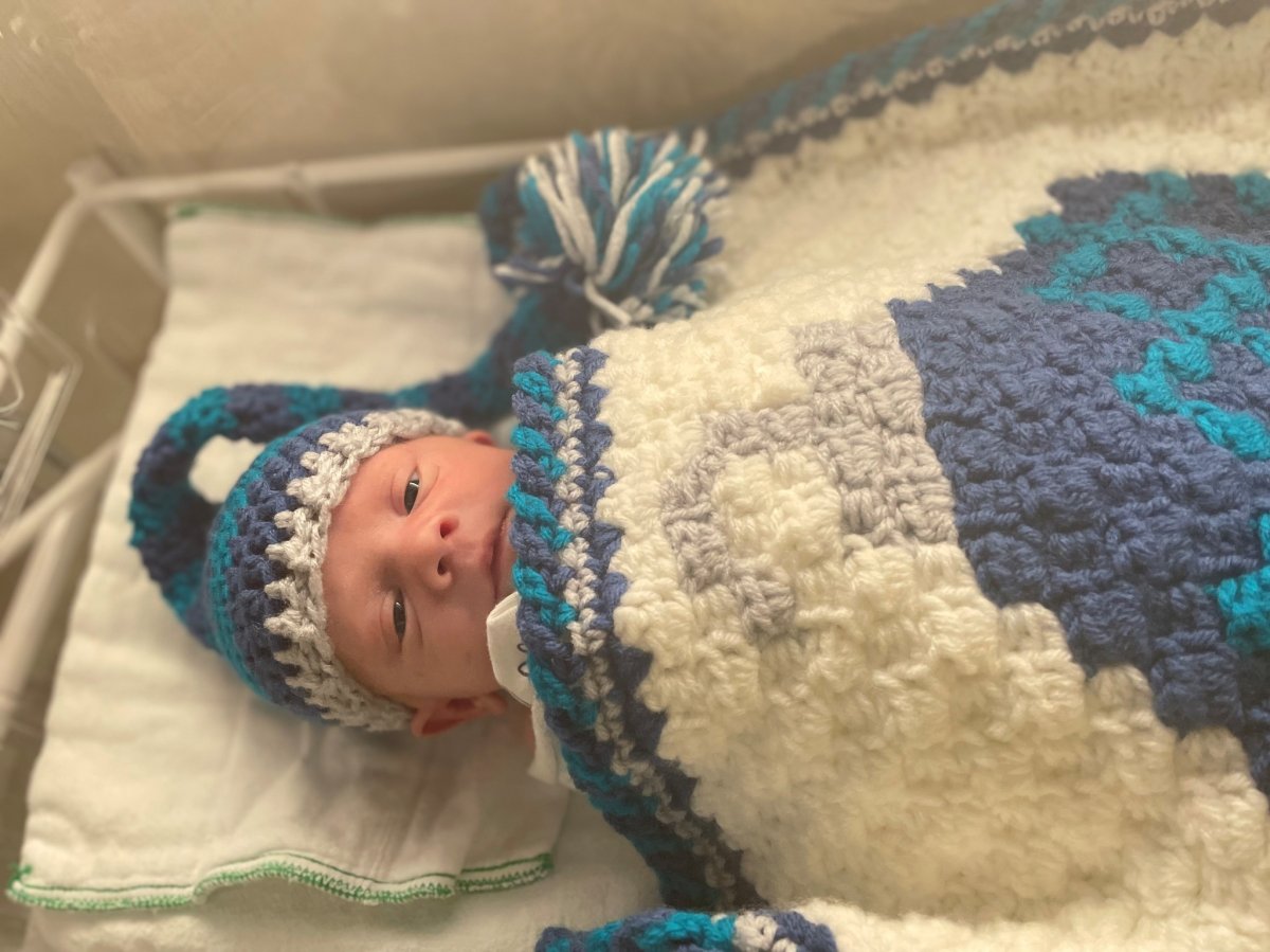 A baby showing off a special holiday outfit and blanket that the NICU Crocheters made. 
