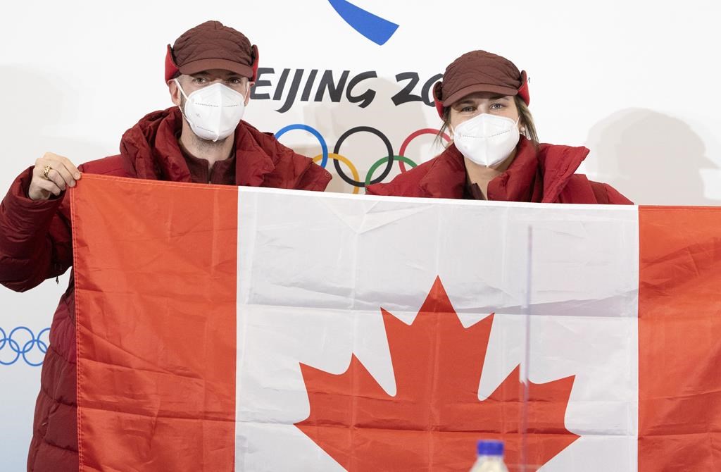 Speedskater Charles Hamelin, left, and hockey player Marie-Philip Poulin hold up the Canadian flag after being named as flag bearers at a news conference Wednesday, February 2, 2022 at the 2022 Winter Olympics in Beijing.