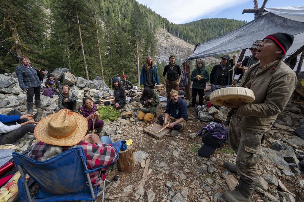 People who have declared themselves “Land Defenders” sing a song as they guard an area of a logging cut block called “Heli Camp” in the Fairy Creek logging area near Port Renfrew, B.C. Monday, Oct. 4, 2021. THE CANADIAN PRESS/Jonathan Hayward.