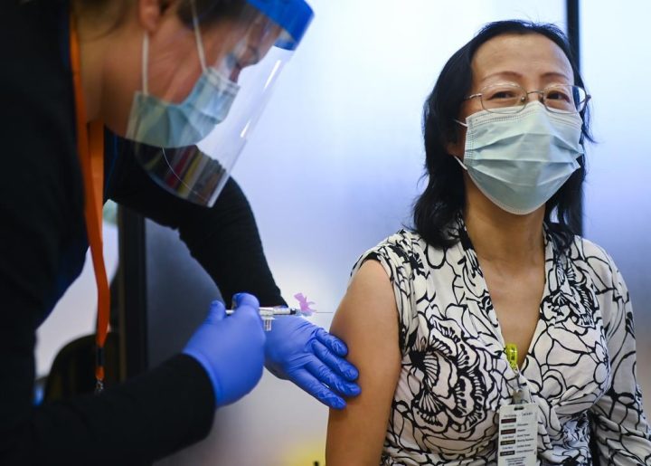 Registered nurse Clair Judd, left, vaccinates LTC nurse Yinghua Fang with the Pfizer-BioNTech COVID-19 mRNA vaccine during the COVID-19 pandemic in Toronto on Tuesday, December 15, 2020. 