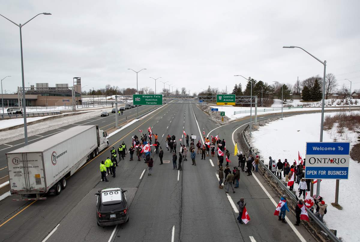 A truck passes Ontario Provincial Police officers and demonstrators in opposition to COVID-19 mandates on the Toronto-bound QEW highway after crossing the Peace Bridge in Fort Erie, Ontario Saturday, February 12, 2022.