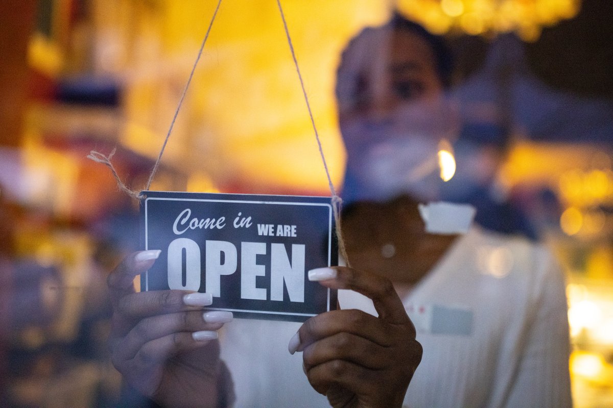 Woman turning an open sign on glass front door of coffee shop. Business owner hanging an open sign at a cafe.