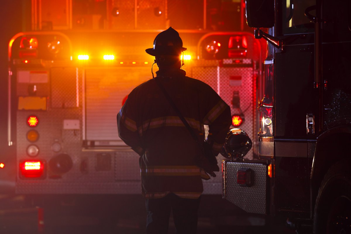 A file image of a firefighter silhouetted against a fire truck with flashing lights at an emergency scene.