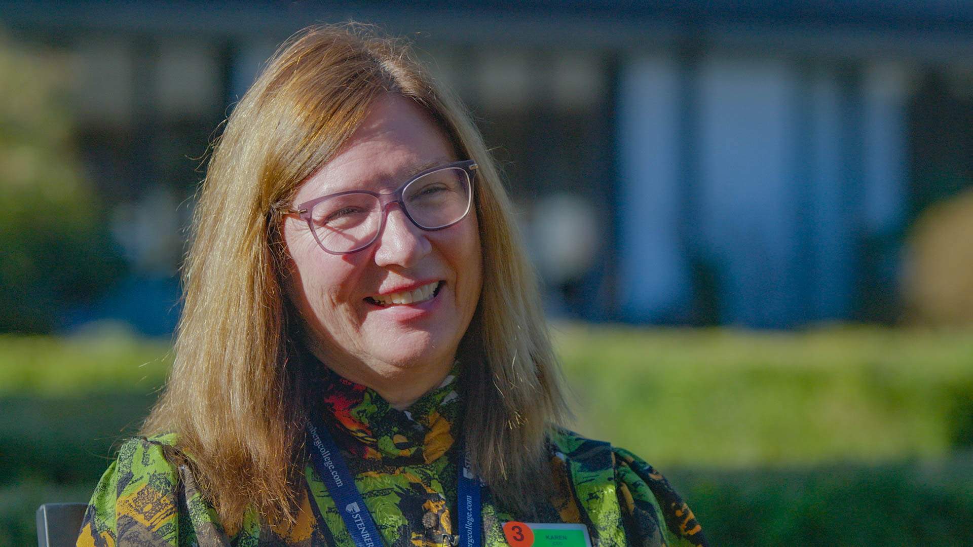 Karen Biggs, a white woman, smiling and looking off camera. She wear glasses and a printed blouse.