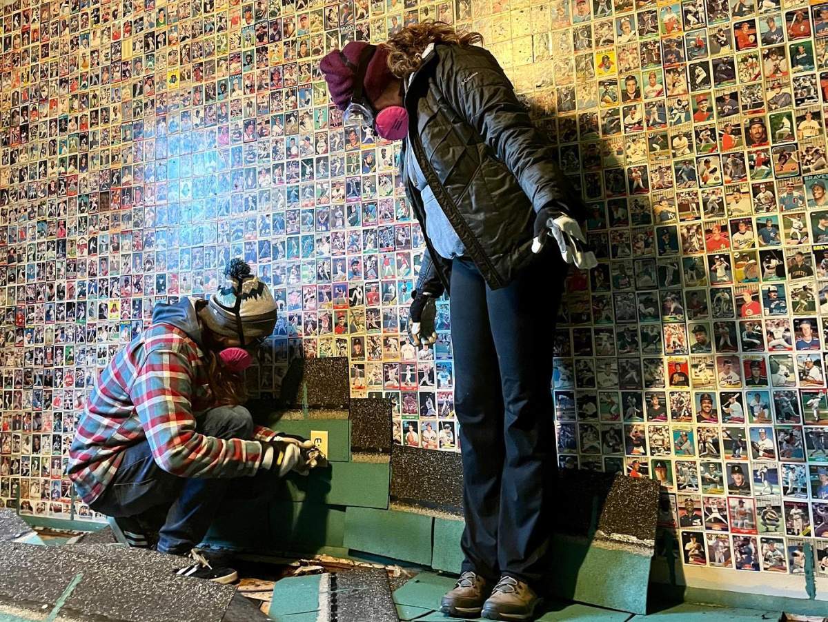 Luke and Melissa Brodt work together to remove the shingles from the wall, revealing the baseball cards.