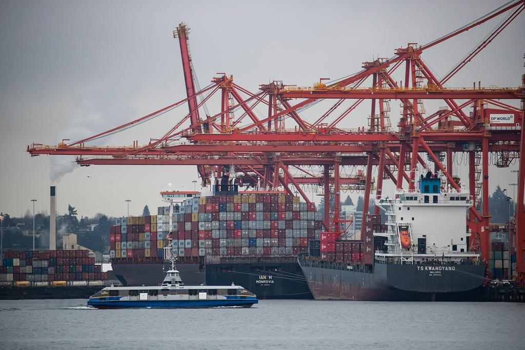 A SeaBus travels across Burrard Inlet as gantry cranes tower above container ships being unloaded and loaded at port, in Vancouver, on Thursday, February 10, 2022. THE CANADIAN PRESS/Darryl Dyck.