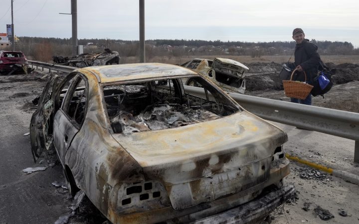 A resident passes by the cars burnt in the Russian shellfire as he flees from his hometown on the road towards Kyiv, in the town of Irpin, some 25 km (16 miles) northwest of Kyiv, Saturday, March 12, 2022.