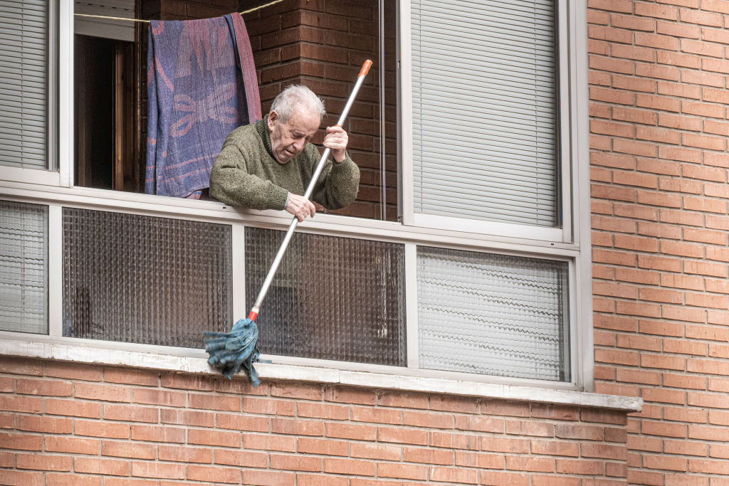An elderly man cleans his window sill with a mop as the city of Burgos wakes up with cars, floors and roofs covered in sand due to the haze.