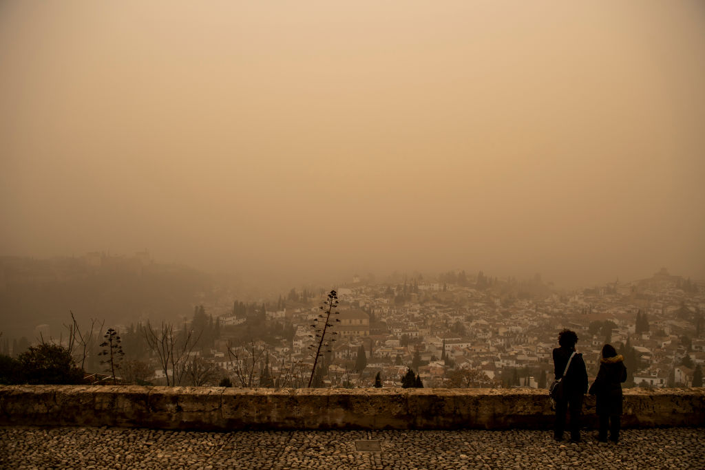 Two tourists look at the Albaicin neighborhood and Alhambra monument almost blurred by the Saharan dust