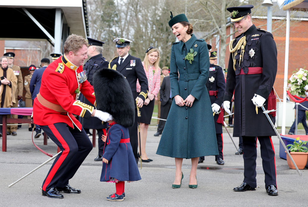 Kate Middleton laughs as she watches a guard put a bearskin hat on a toddler.