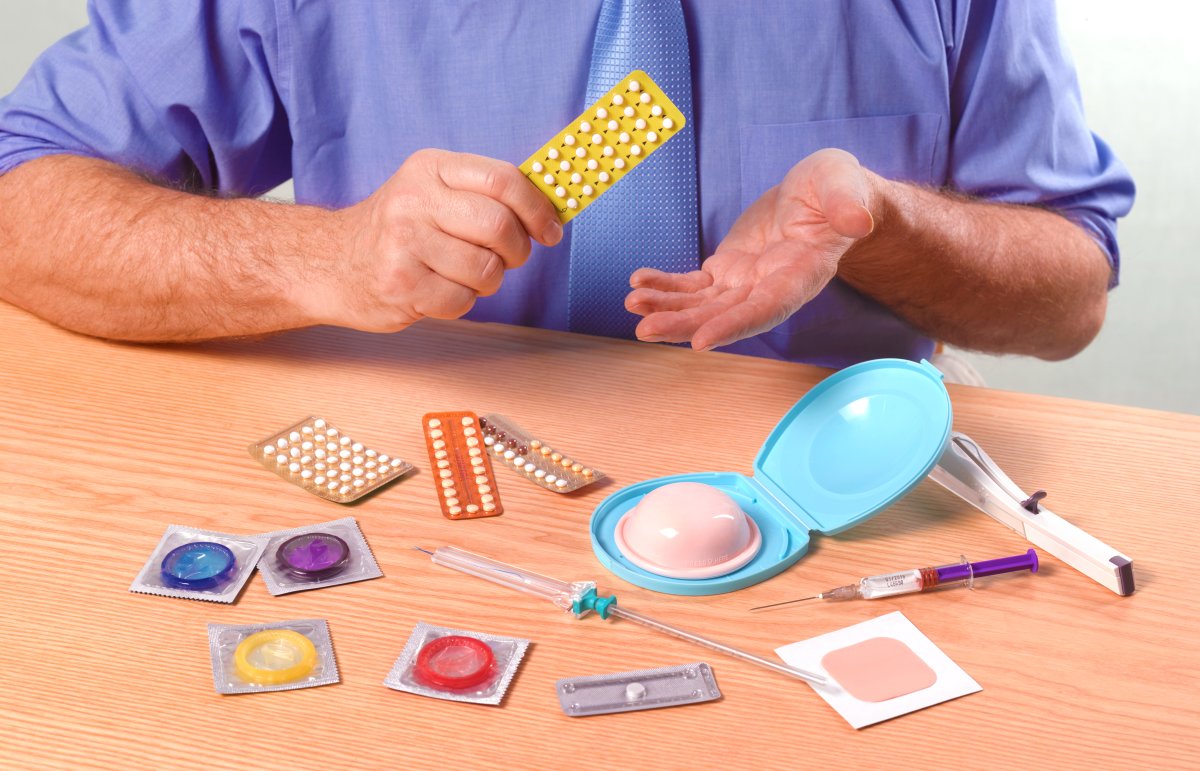 Doctor explaining contraception, with several forms of contraceptives on the table, including condoms, dental dams and oral pills.