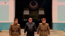 North Korean leader Kim Jong-Un is seen flanked by two military officials. A large ICBM is seen in the background.