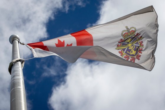 The flag of the Canadian Armed Forces flies against a cloudy sky.