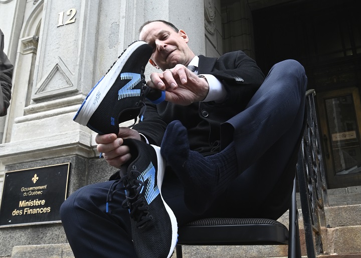 Quebec Finance Minister Eric Girard puts on a pair of running shoes as he responds to reporters questions on the eve of a budget speech, Monday, March 21, 2022 in front of the finance ministry in Quebec City. 