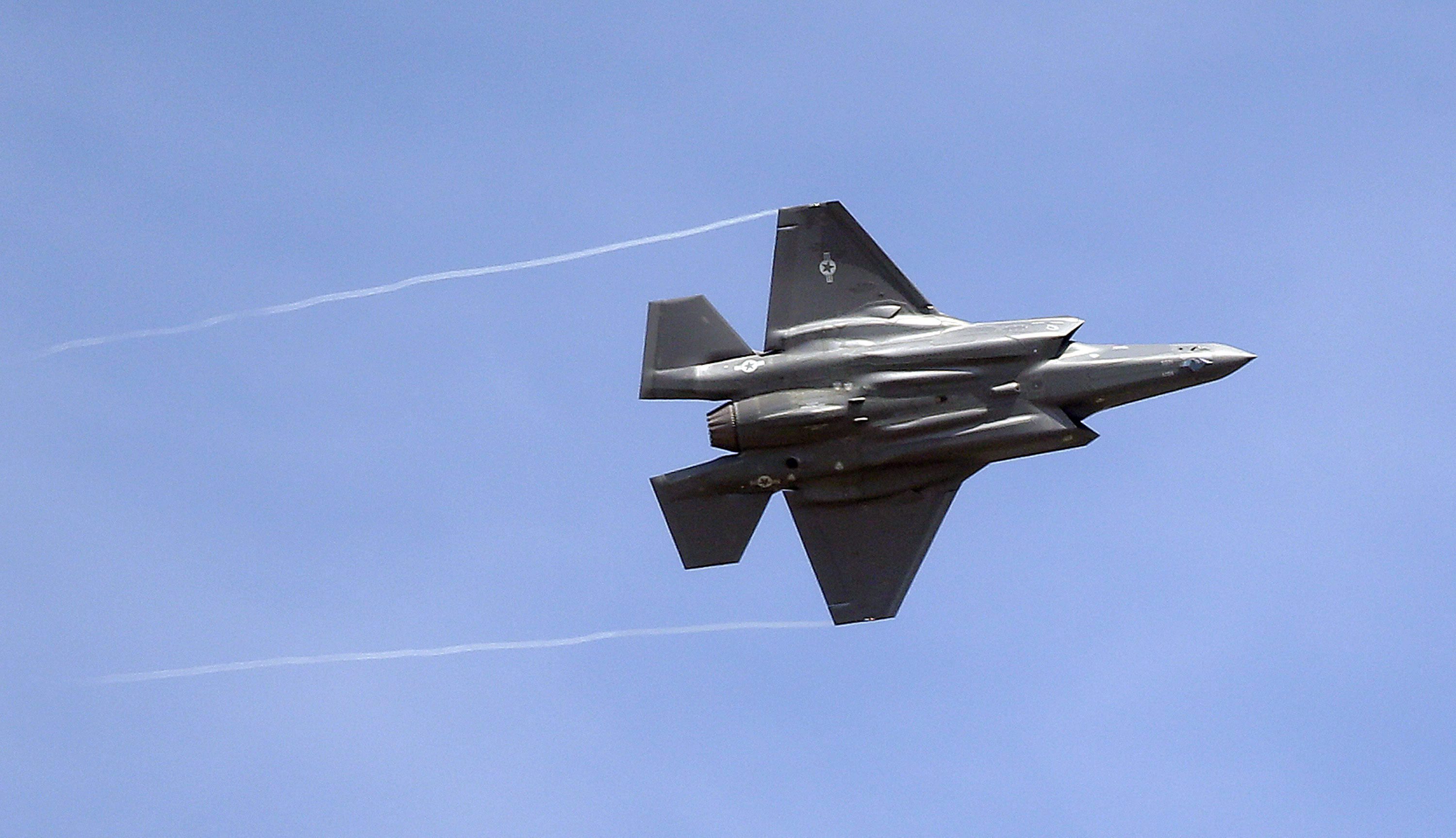 A Lockheed Martin F-35 fighter jet flies against a cloudless blue sky.