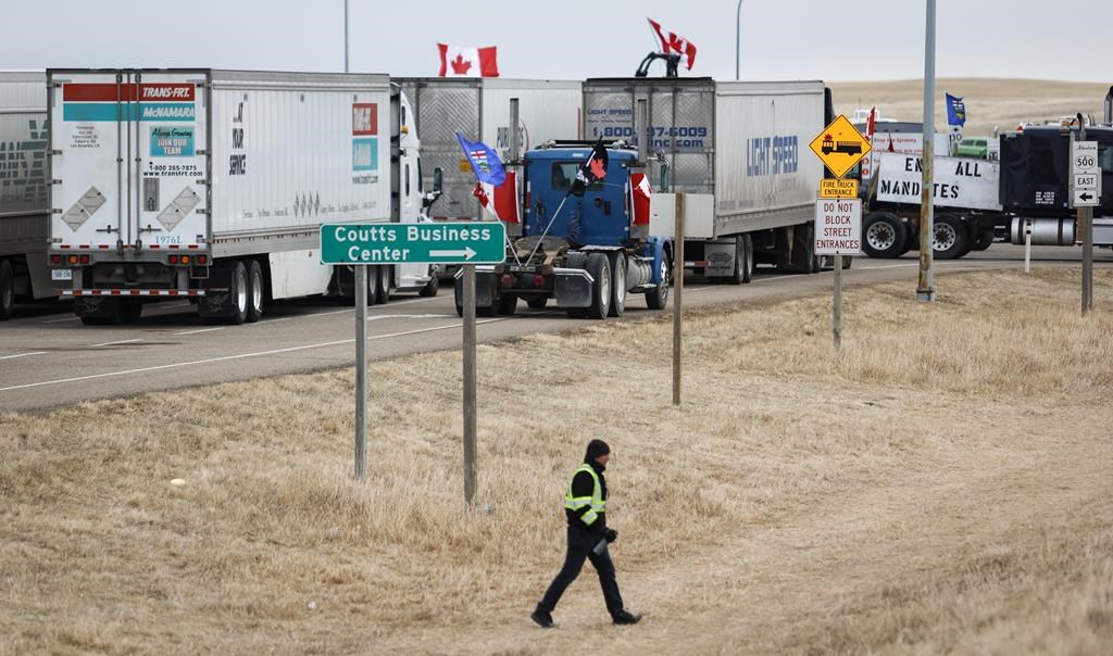 Anti-mandate demonstrators gather as a truck convoy blocks the highway at the busy U.S. border crossing in Coutts, Alta., Monday, Jan. 31, 2022. One of four men charged with conspiracy to commit murder at a border blockade protest in southern Alberta has run into a roadblock in his desire to set an early trial date. THE CANADIAN PRESS/Jeff McIntosh.