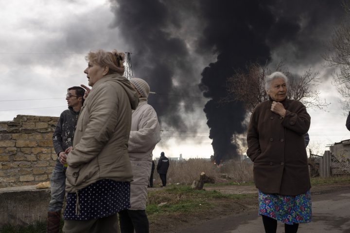 People stay in a yard as smoke rises in the air in the background after shelling in Odessa, Ukraine, Sunday, April 3, 2022.