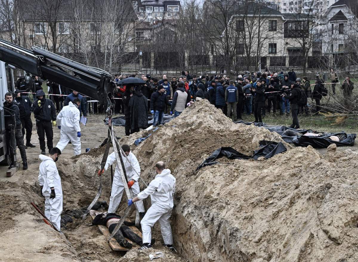Ukrainian investigators exhume bodies form a mass grave in the gardens of the St Andrew church in the town of Bucha, northwest of Kyiv, on April 8, 2022, during Russia's military invasion launched on Ukraine. - Ukrainian investigators began to exhume a mass grave in Bucha on April 8, opening the early stages of what police say will be a war crimes probe targeting Russian troops who occupied the Kyiv commuter town. The grave -- a long deep trench in the mud behind a gold-domed church -- was used by Ukrainians to bury neighbours they claim were killed at the hands of Russian armed forces which arrived on February 26.