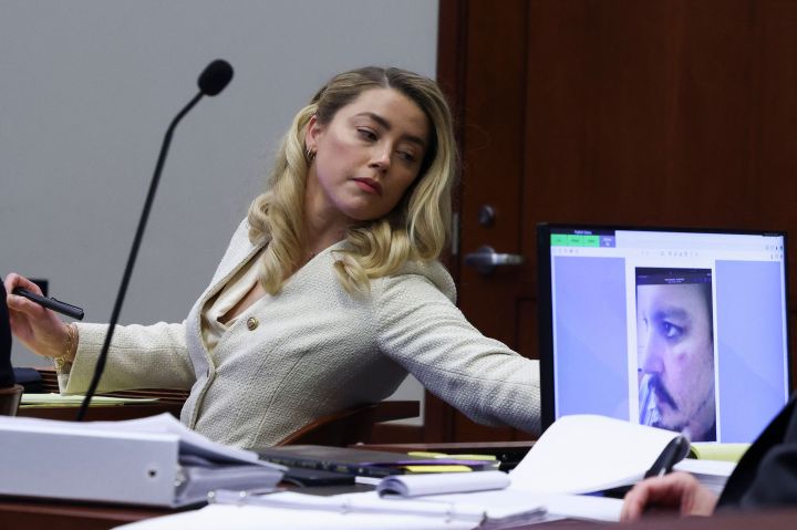 Actress Amber Heard listens to her ex-husband Johnny Depp, as a picture of an injury to his face is seen on a screen, during his defamation trial against her at the Fairfax County Circuit Courthouse in Fairfax, Va., April 20, 2022.