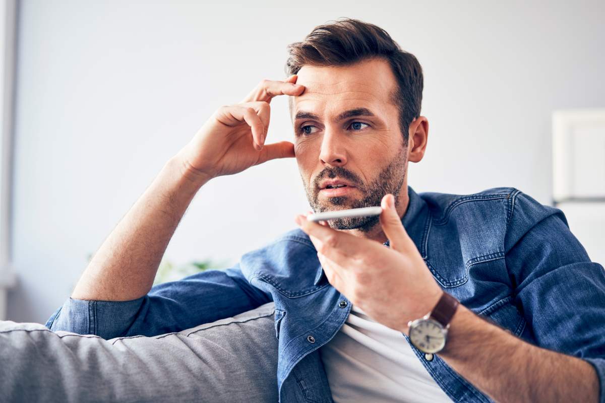 Worried man sitting on sofa using cell phone