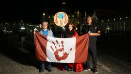 Palexelsiya Lorelei Williams raises the drum her father designed as Sts'ailes First Nation Chief Ralph Leon and Coun. Kelsey Charlie hold up the genocide flag of Canada in front of St. Peter's Basilica on Tues. March 29, 2022.