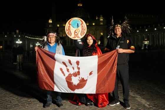 Palexelsiya Lorelei Williams raises the drum her father designed as Sts'ailes First Nation Chief Ralph Leon and Coun. Kelsey Charlie hold up the genocide flag of Canada in front of St. Peter's Basilica on Tues. March 29, 2022.