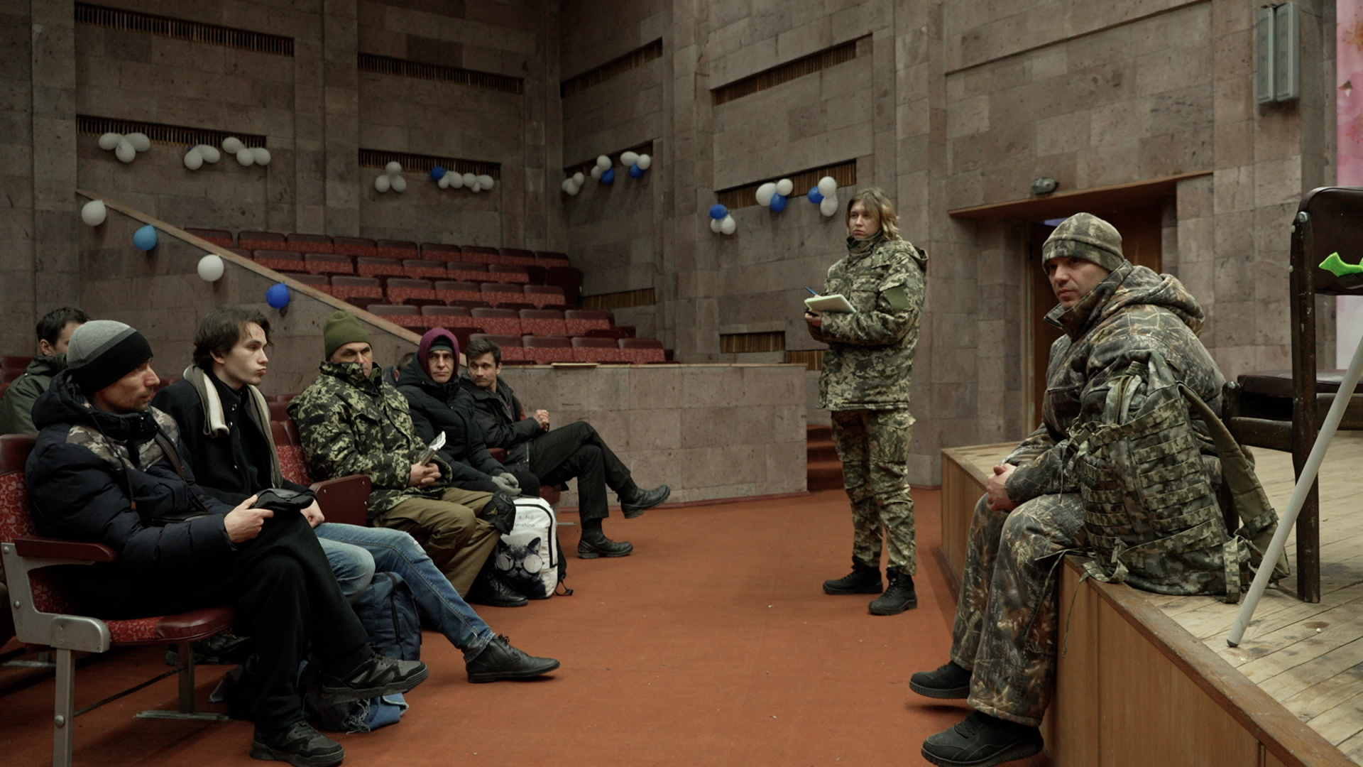 New recruits gather in an auditorium for training. Olena Lypovenko stands at the front.