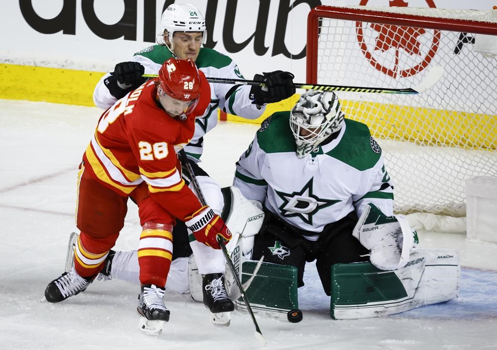 Dallas Stars goalie Jake Oettinger, right, covers his net as Calgary Flames centre Elias Lindholm, centre, tries to score while being checked by Stars centre Roope Hintz during second period NHL playoff hockey action in Calgary, Tuesday, May 3, 2022.THE CANADIAN PRESS/Jeff McIntosh.
