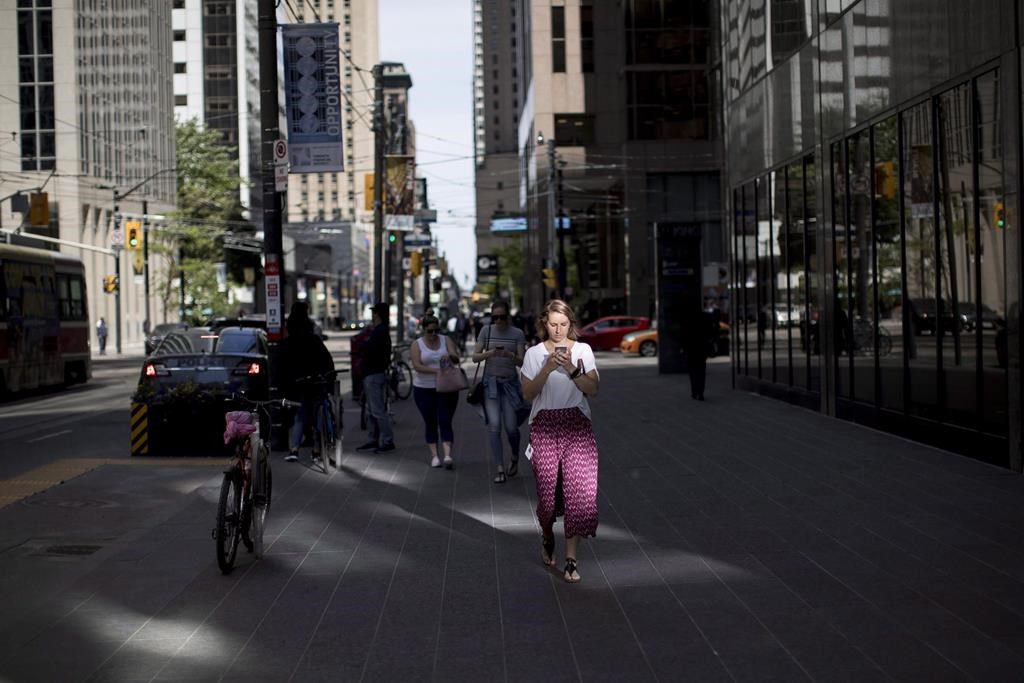 A woman looks down at her cell phone while walking though downtown Toronto, on Tuesday, June 12, 2018.